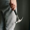 Crop unrecognizable male in casual clothes holding metal hammer with rubber handle in room