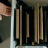 Top view of assorted wooden panels neatly arranged in a drawer with a hand reaching out.